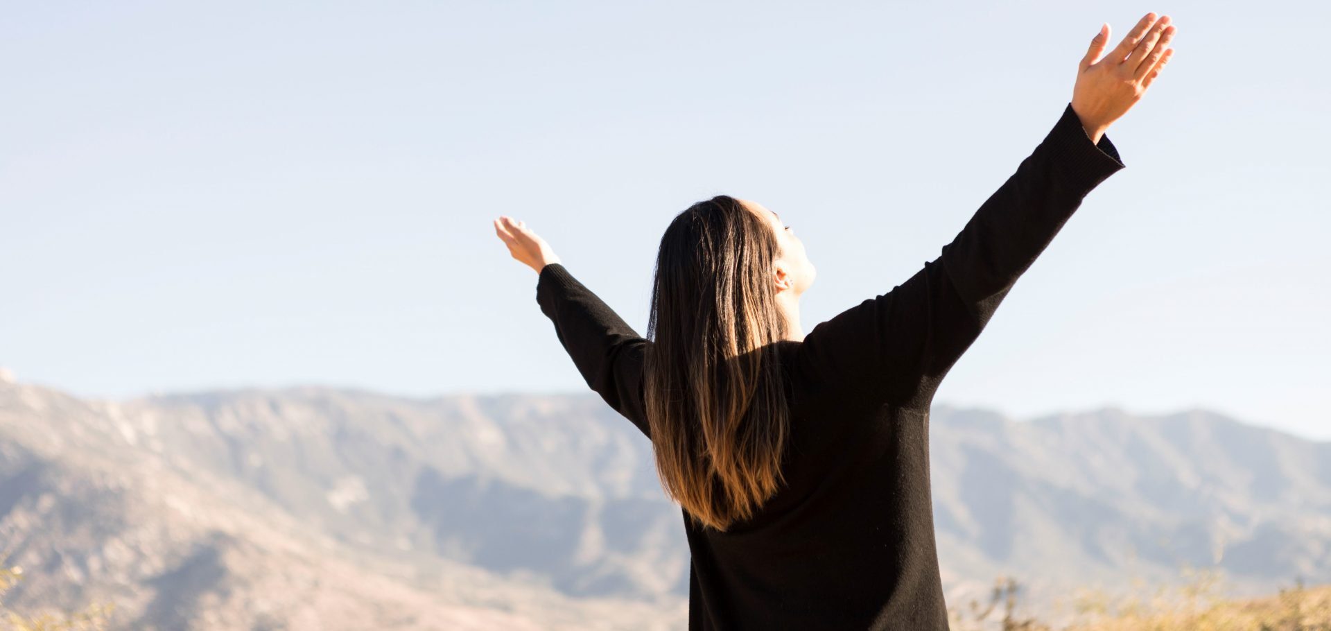 Woman looking at desert mountains raising hands up