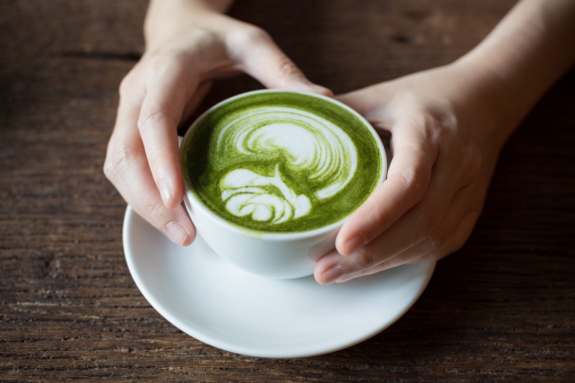 hands holding a cup of matcha and almond milk latte