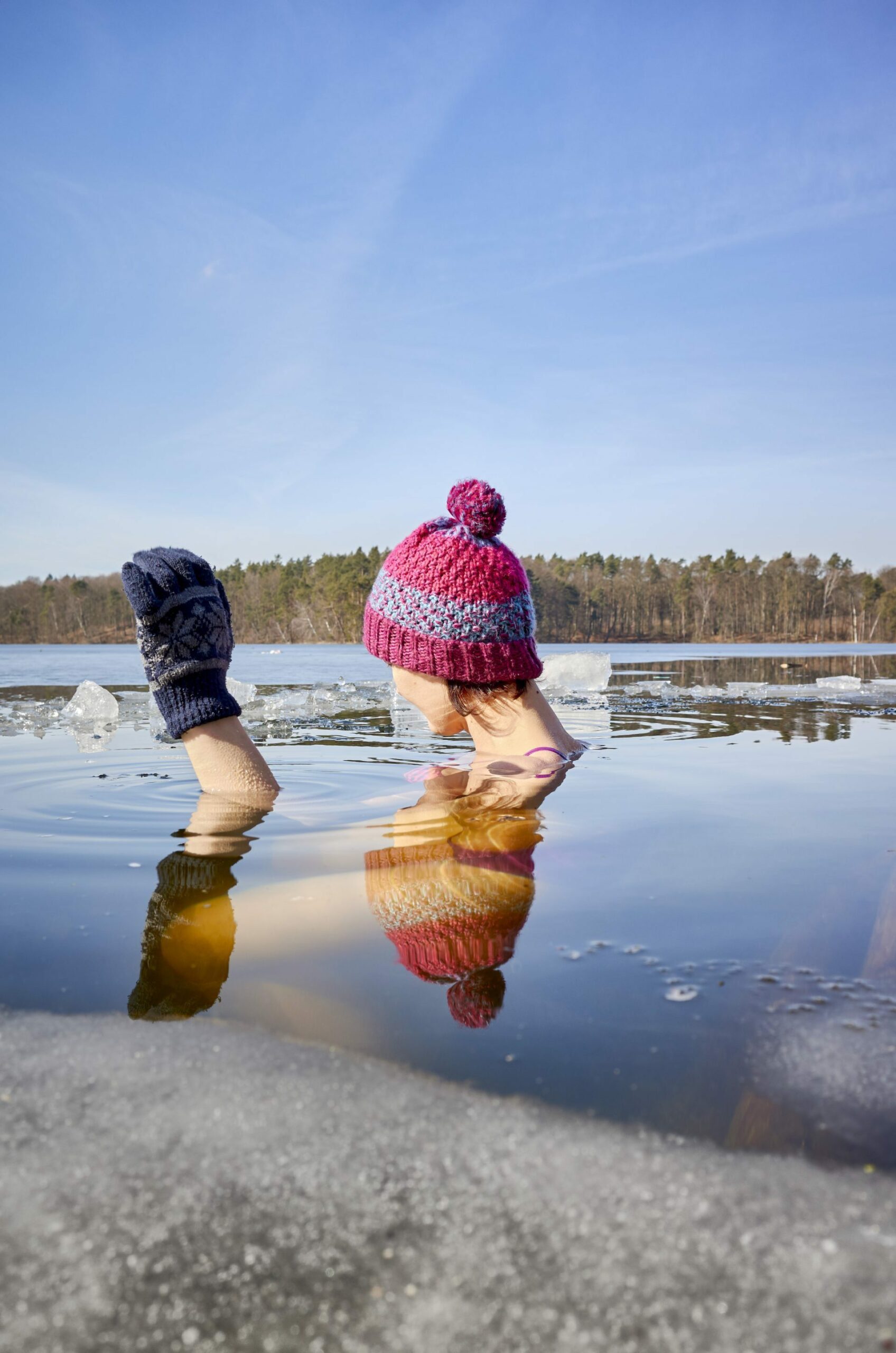 Person going swimming in cold lake wearing gloves and toque