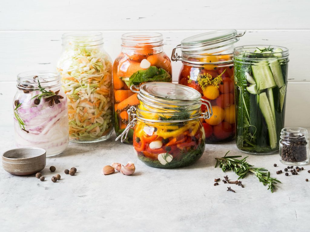 A selection of pickled vegetables like cucumbers, tomatoes, carrots, peppers, slaw and onion in jars