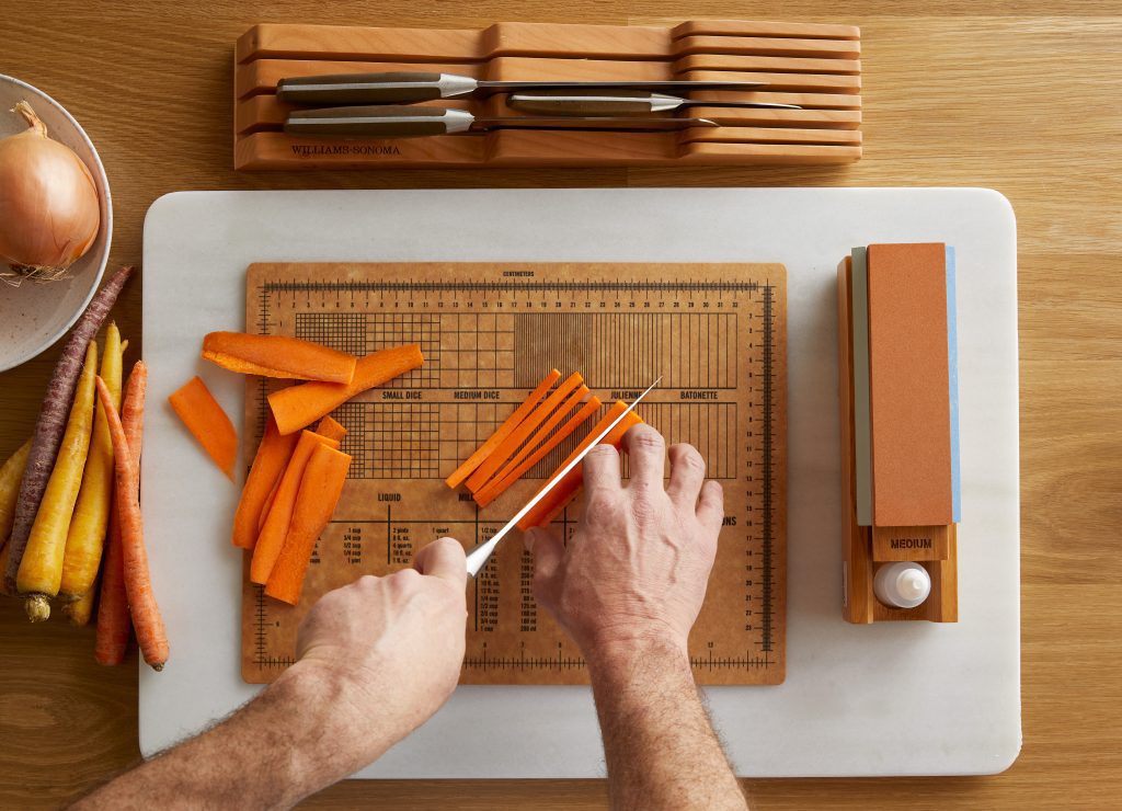 Hands cutting carrots on cutting board with knife