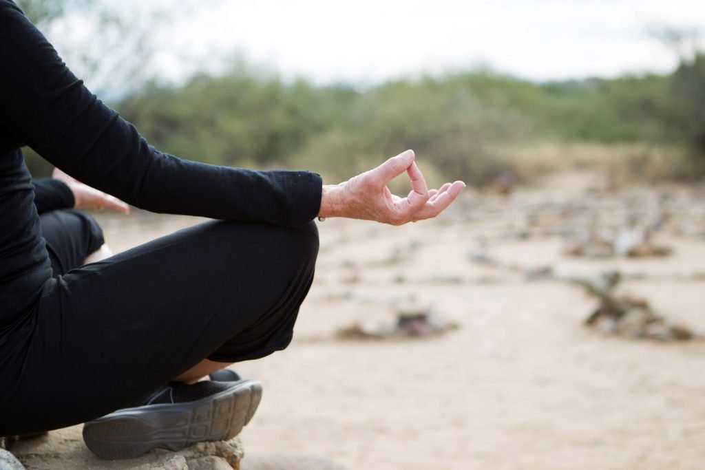 person sitting a rock cross legged with hands in meditative state