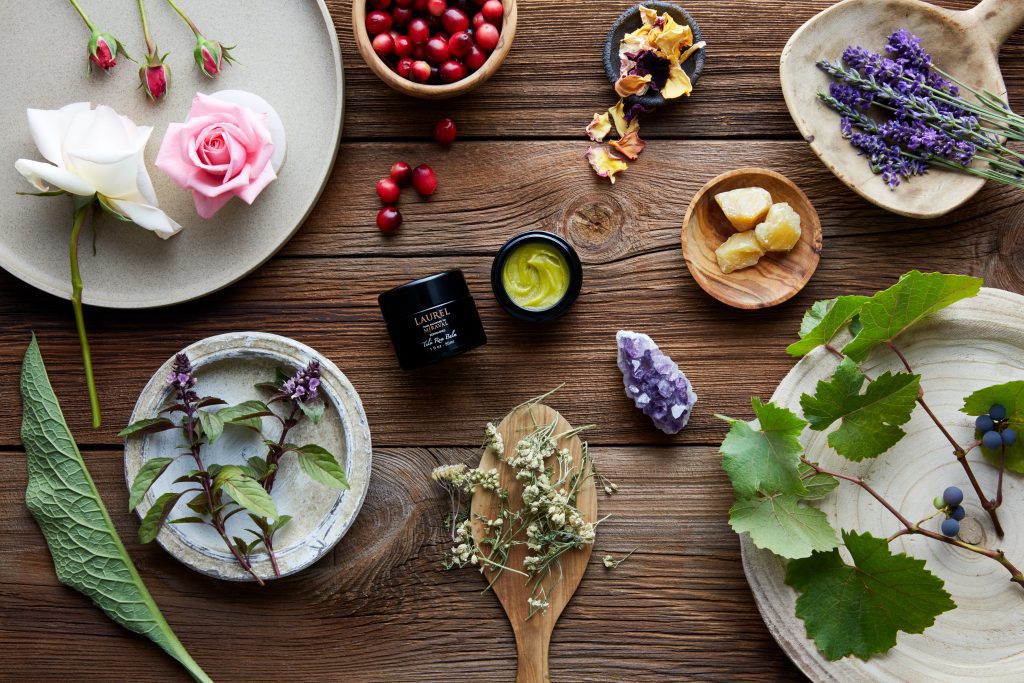 Miraval Tulsi Rose Balm on wood with roses, crystals, lavender, leaves tulsis, cranberries