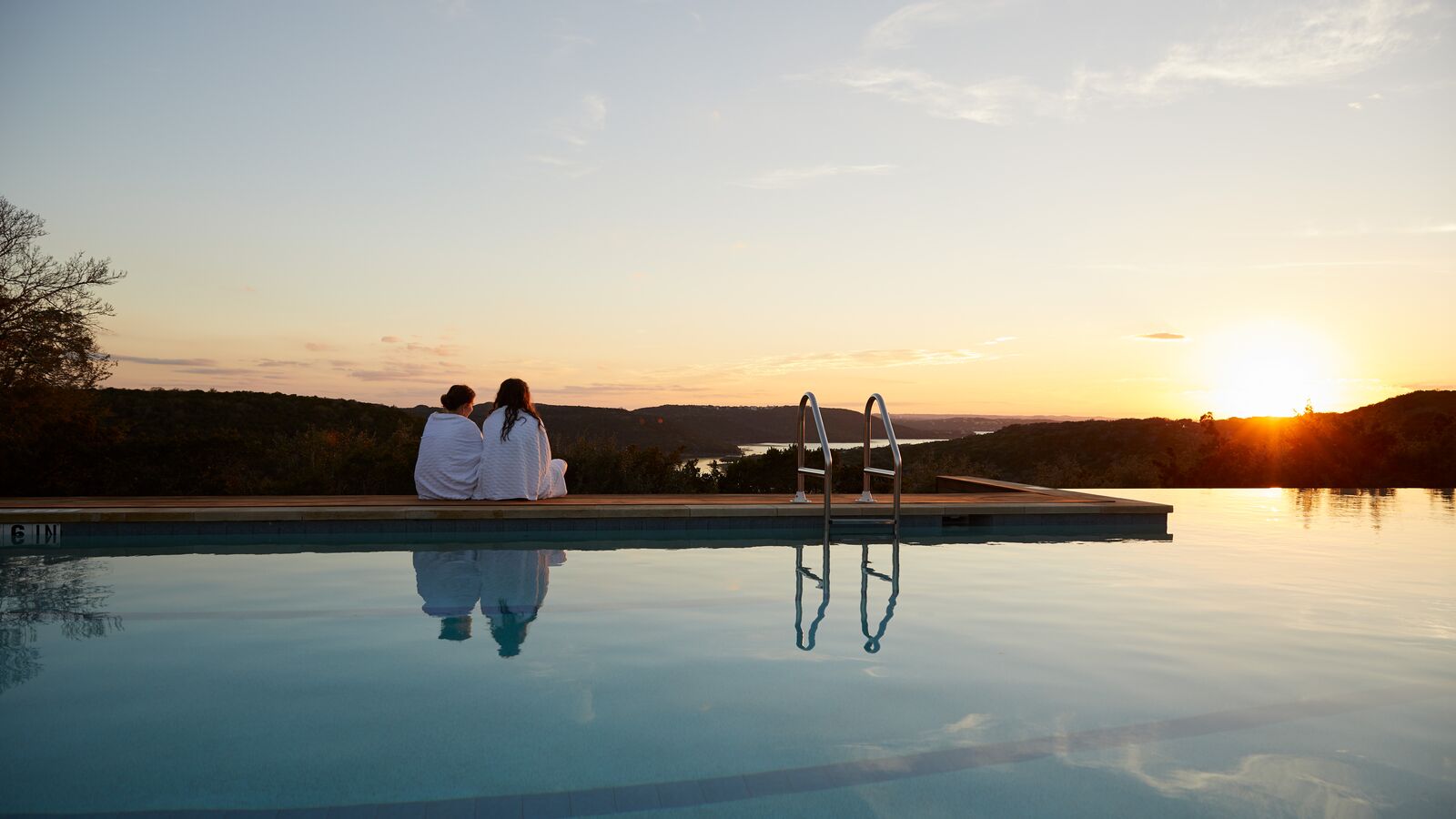 two people in robes watching the sun set by the pool